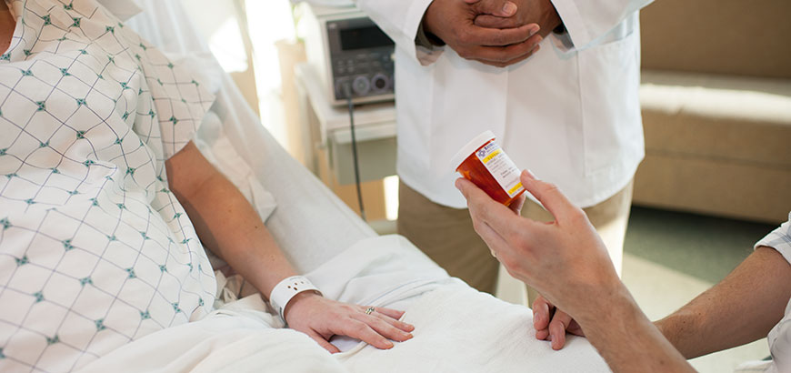 Close up of a medication bottle being handed to a patient in a hospital bed with a doctor watching in the background