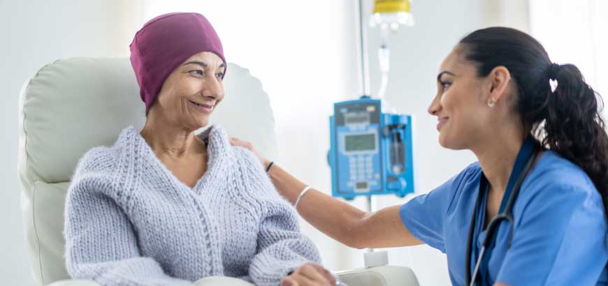 A cancer patient in a hospital bed is comforted by a nurse