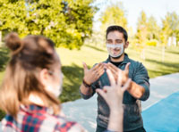 A man wears a clear face mask so the person he is talking to can see his lips move, and uses sign language to have a conversation