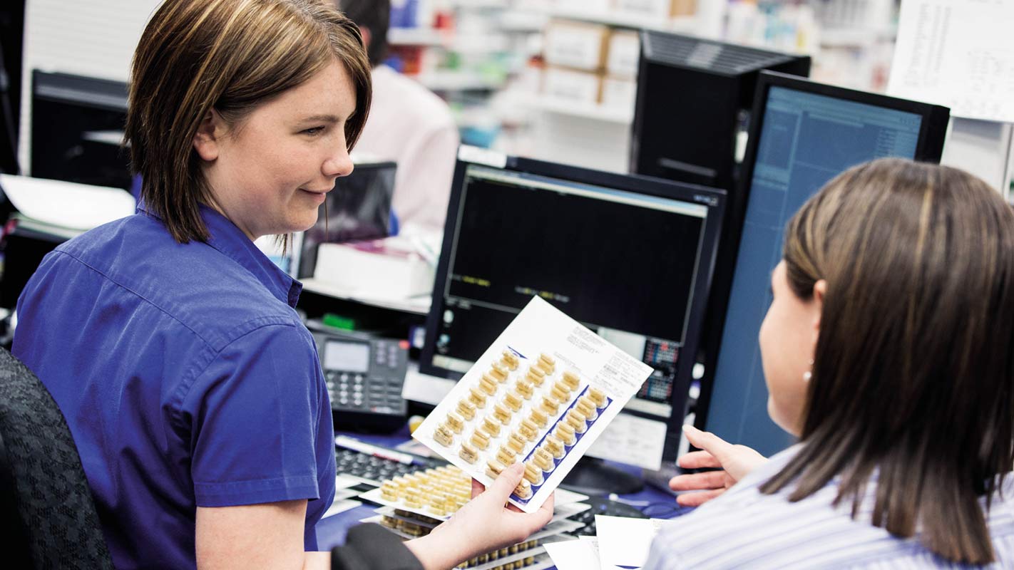 A pharmacy technician handing a pharmacist medication pills