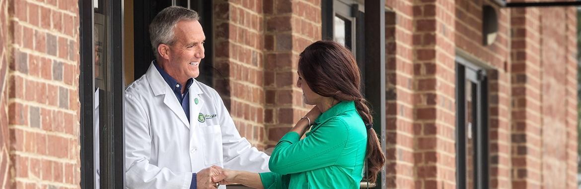 Woman and man standing outside doorway of brick building shaking hands and smiling