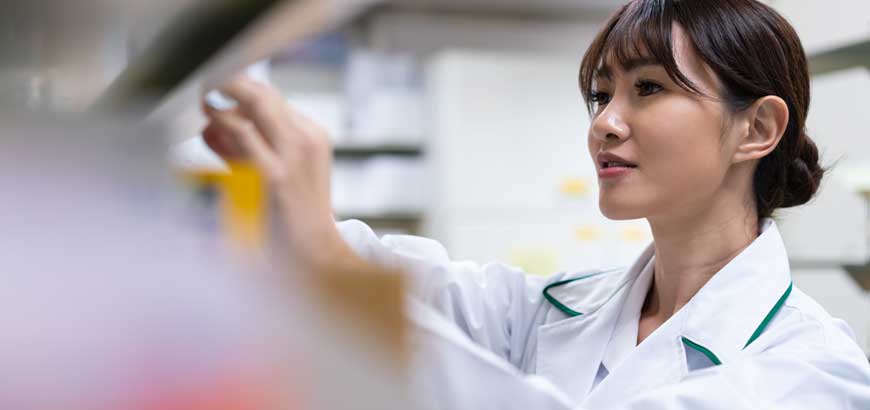 A female pharmacist reaches for a shelf of medication