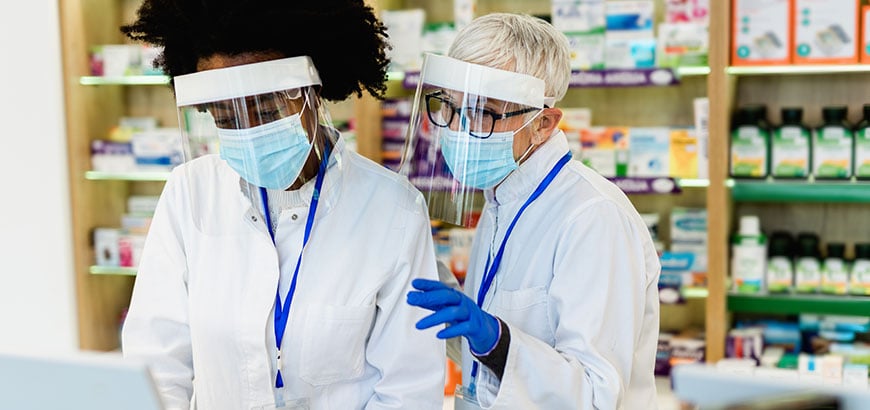 Two pharmacists working in a pharmacy wearing viral protective gear