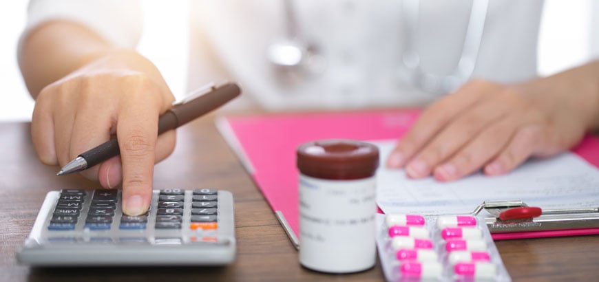 Close up of hands on a desk with a calculator and package of medication