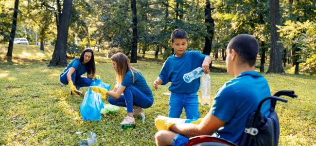 Two women, a child and a man in a wheelchair work together to collect litter at a park