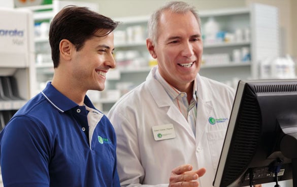 Two male pharmacists smile and chat while looking at a computer screen in a Health Mart Pharmacy.