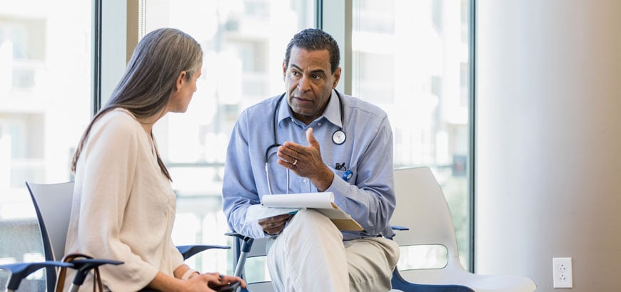 A doctor with a stethoscope is consulting with a seated woman in a bright office.