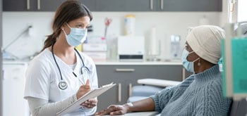 A physician writes on a clipboard as she speaks to a patient