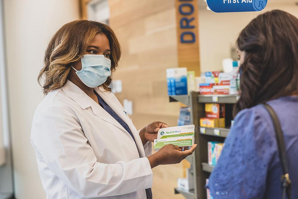 A pharmacist holding a medication and speaking with a customer