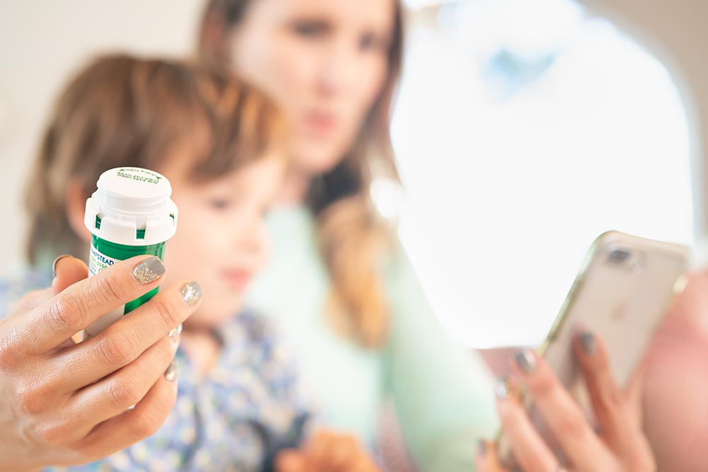 A woman sitting with her child using a cell phone and holding a prescription pill bottle